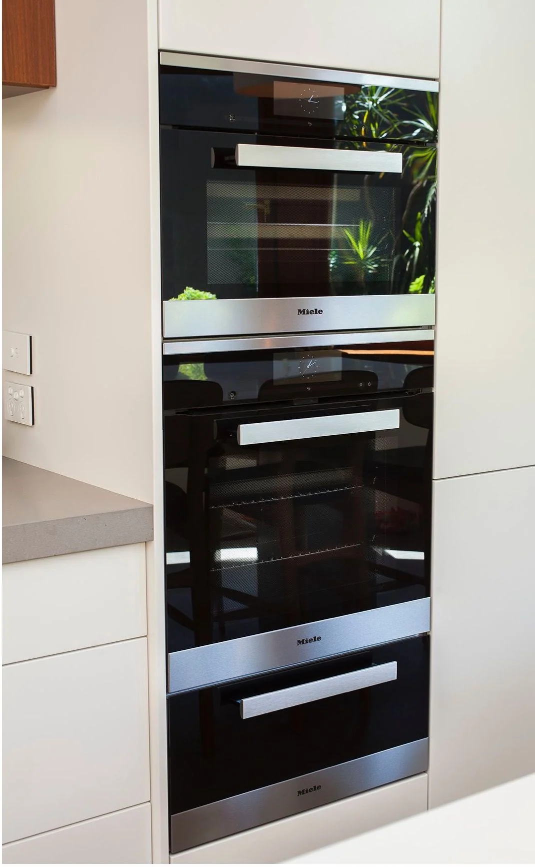 Two built-in ovens and a warming drawer stacked in a tall kitchen cabinet