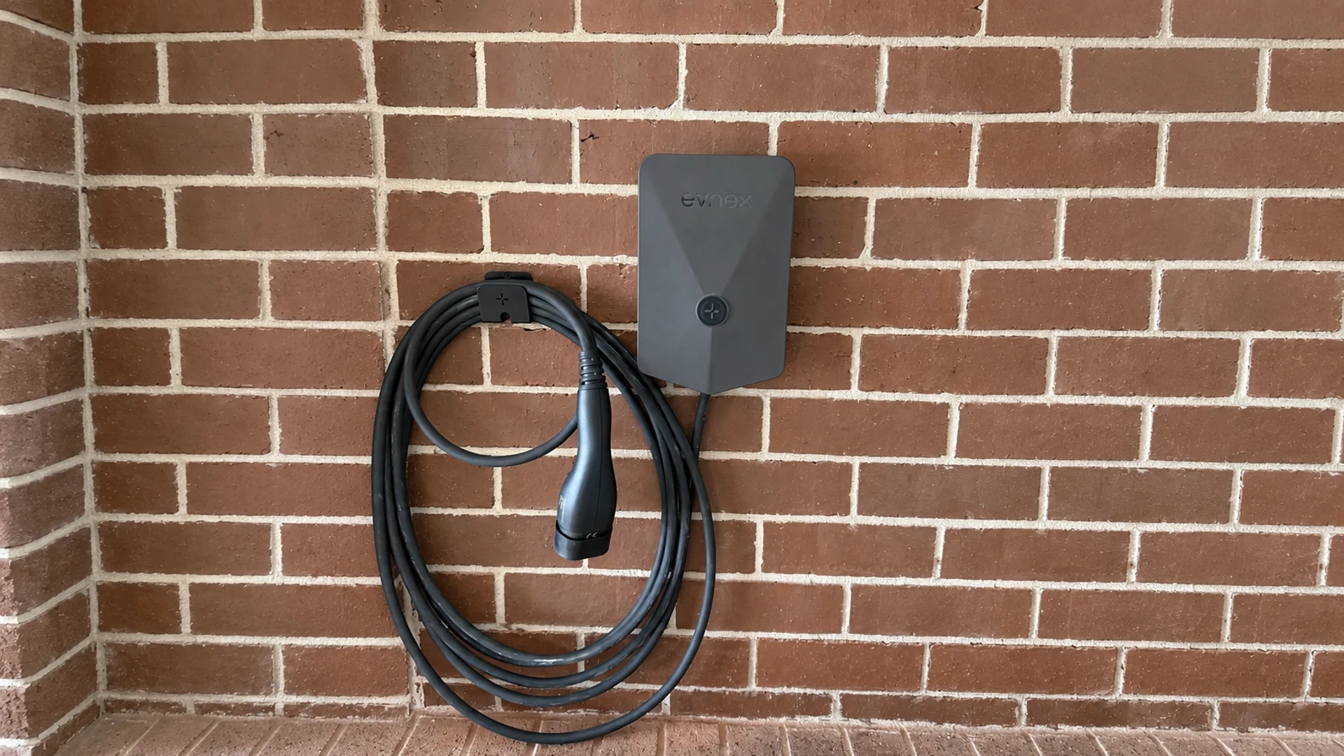 Evnex home EV charger on brickwork, with two curved status lights beside its centre emblem