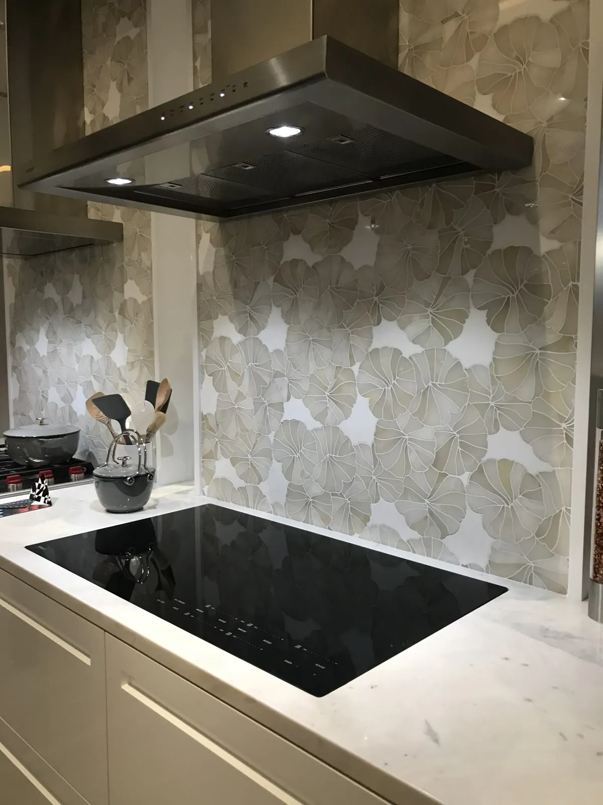 Black induction cooktop set into a white stone benchtop under a stainless rangehood