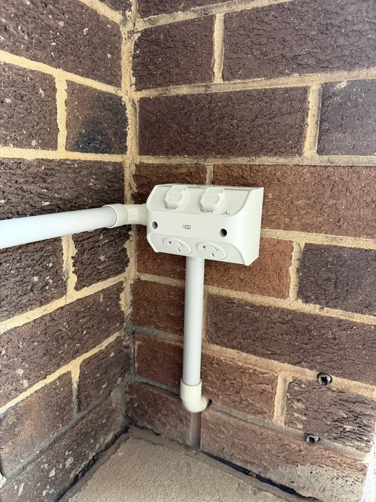 Weatherproof double power point with switch covers, wired in conduit on a brick wall