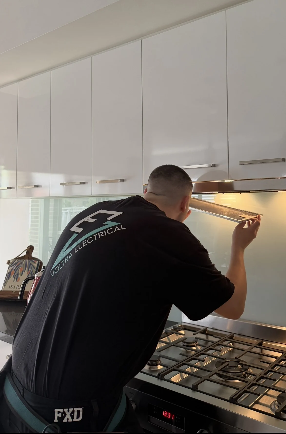 Voltra electrician working on a kitchen rangehood above a cooktop