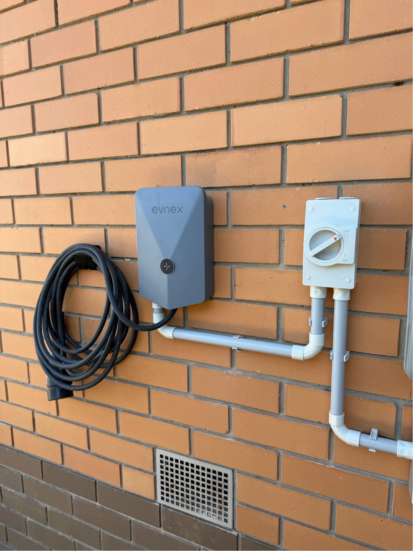 Light-coloured Evnex charger with conduit and isolator installed on brickwork at the Thomastown project